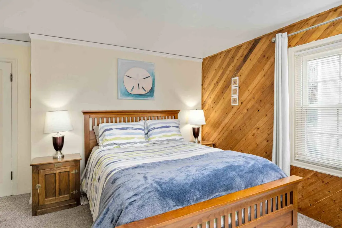 A tranquil bedroom with a cozy bed, bedside lamps, soothing artwork, and warm wood paneling. The space exudes calm and privacy, inviting guests to relax, read, or enjoy a quiet morning in bed.