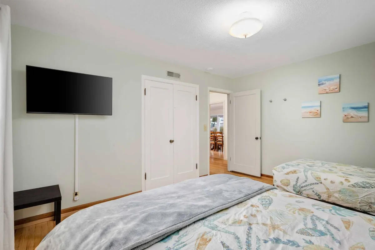 A soothing bedroom with floral bedding, a mounted television, and decorative wall art. The room feels bright and inviting, with gentle touches of coastal charm and practical amenities for unwinding.
