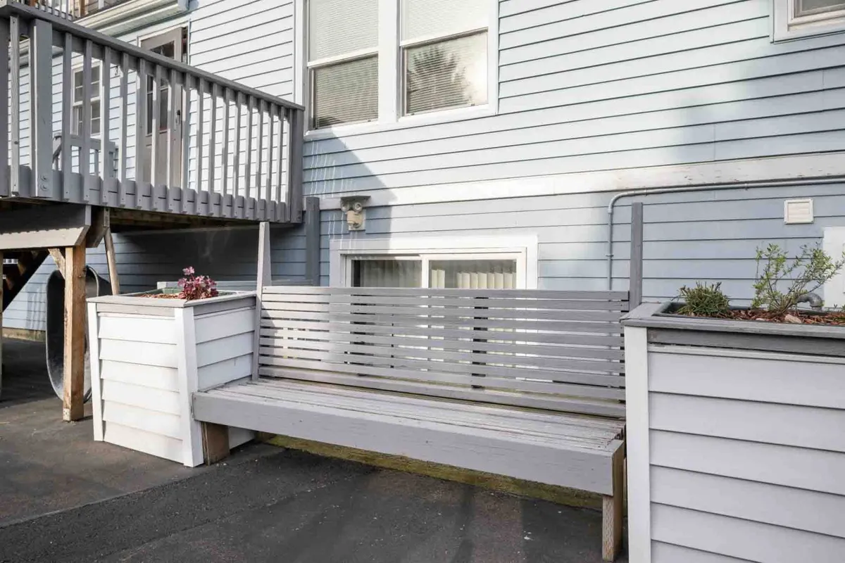A cozy exterior patio scene with a wooden bench and planter boxes provides a casual, outdoor relaxation spot. The area looks inviting for guests (and their pups) to unwind and socialize, with natural light adding warmth to the scene.