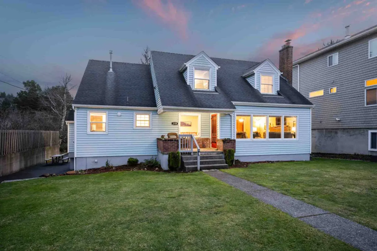 The exterior of the home featuring a welcoming front porch, large windows that hint at ocean views, and a manicured lawn. The porch is ideal for relaxing, with the surrounding greenery enhancing the sense of peace and connection to the outdoors.