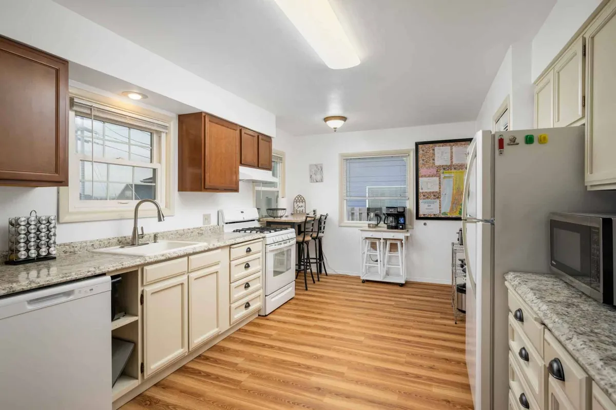 This image highlights a kitchen with granite countertops, warm wood cabinets, and visible appliances. The open-plan design connects the kitchen to a dining area, creating a welcoming and functional space. The scene evokes a lively atmosphere, with indications of cooking, family meals, and social activity.