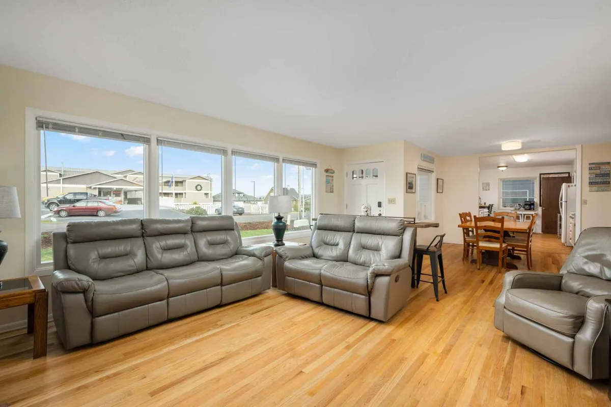 This bright, open interior scene centers on a spacious living area furnished with leather recliners, a large dining table, and expansive windows that flood the room with natural light and frame sweeping ocean views. The setup invites socializing and relaxation, perfectly embodying the heart of the home's communal space.
