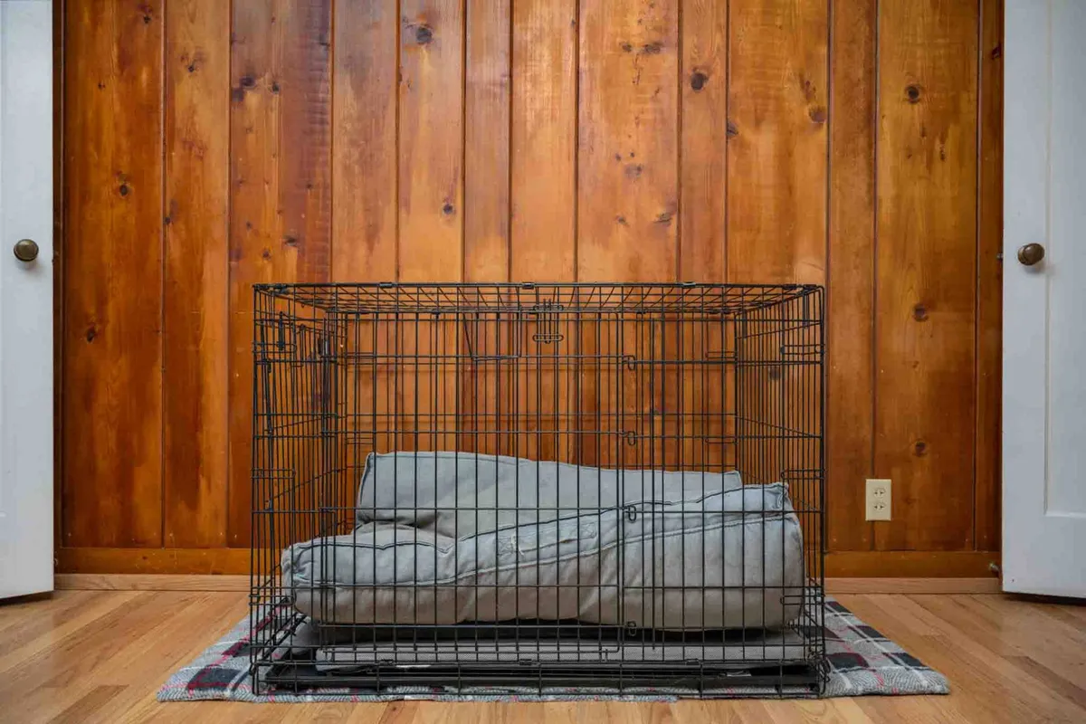 An interior shot featuring a cozy wire dog crate set against a wooden wall and a plaid rug, creating a welcoming and safe environment for pets. The space is clearly prepared for four-legged family members, reinforcing the pet-friendly policy.