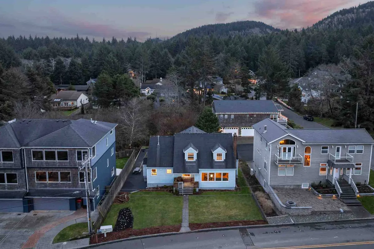 A warm, inviting image of a house with glowing lights surrounded by lush greenery, neighboring homes, and mountains in the distance, suggesting a peaceful community environment ideal for family bonding and evening strolls.