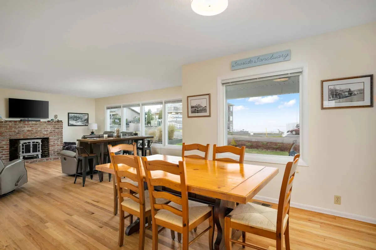 A welcoming dining area set beside large windows that overlook the coastline, with a fireplace nearby. The arrangement encourages lingering over meals while enjoying sunset views and the warmth of the fire, reinforcing the room's inviting, communal atmosphere.